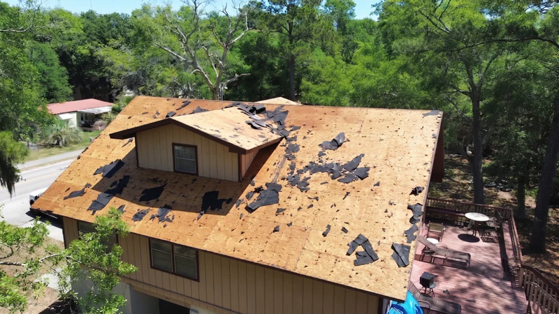 Bare roof deck mid-tear-off on a Hilton Head Island home, full-home oblique angle showing dormer and street