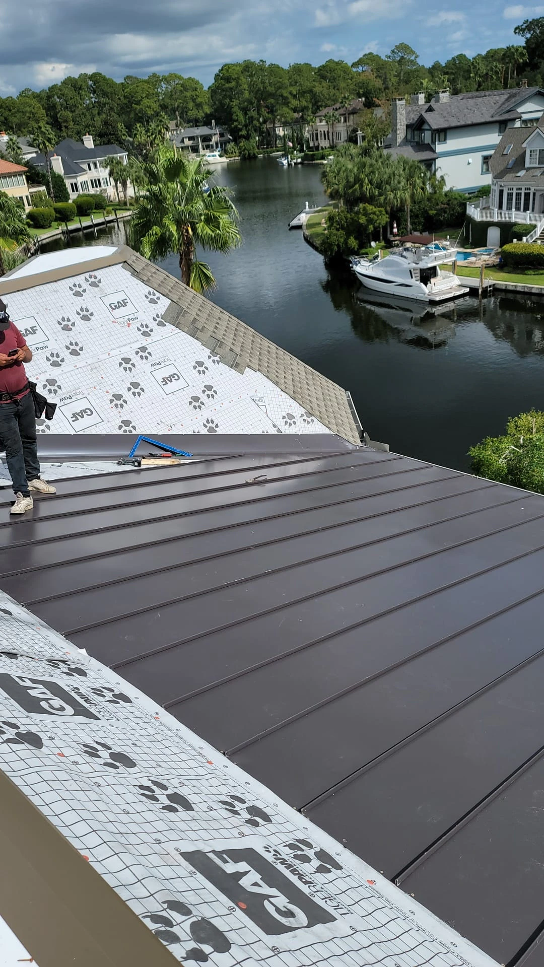 Aerial view of a standing-seam metal roof on a Lowcountry plantation home, marsh and palms behind